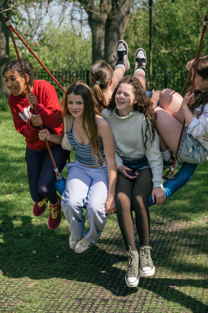 Teenage girls on basket swing in park